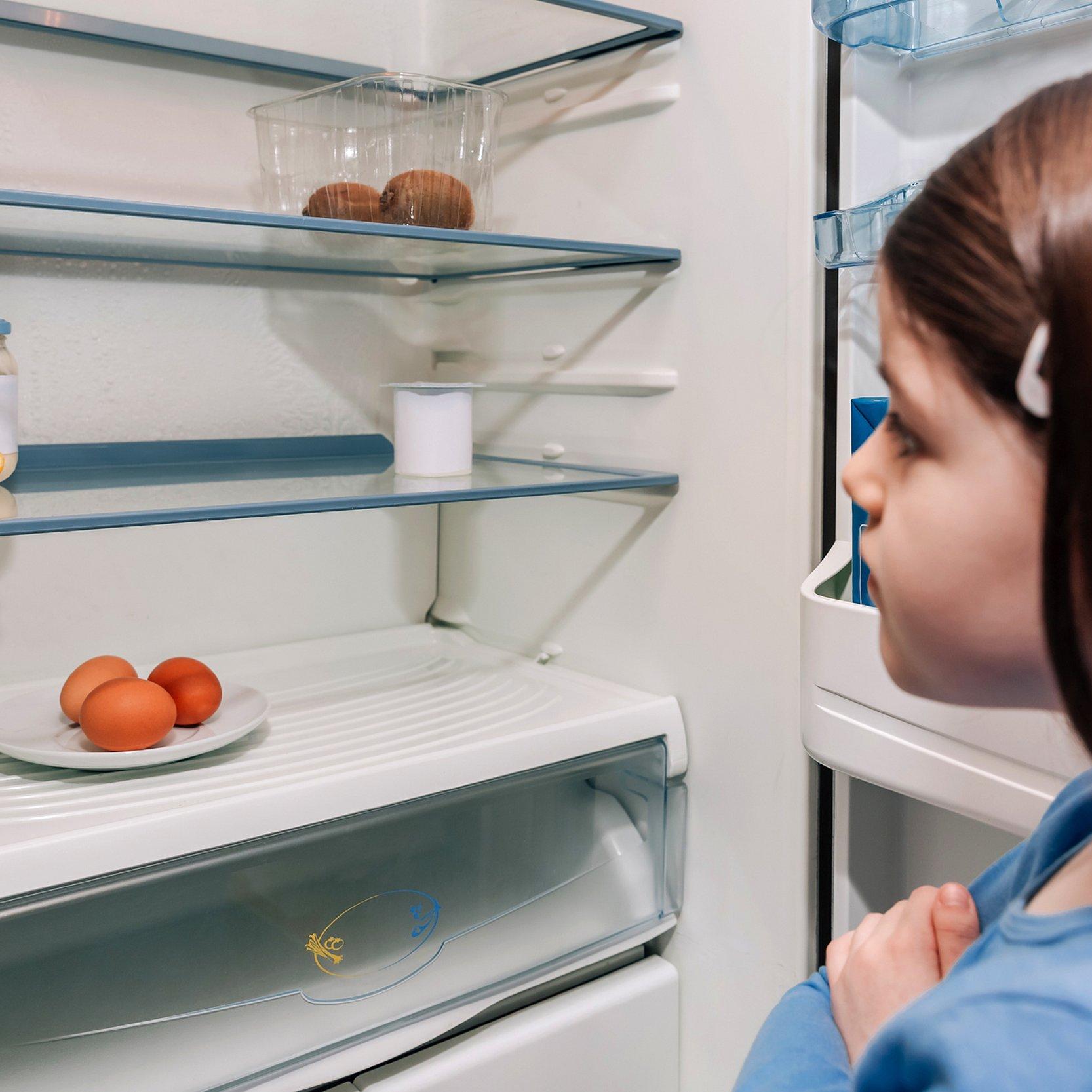 Mädchen schaut in fast leeren Kühlschrank.