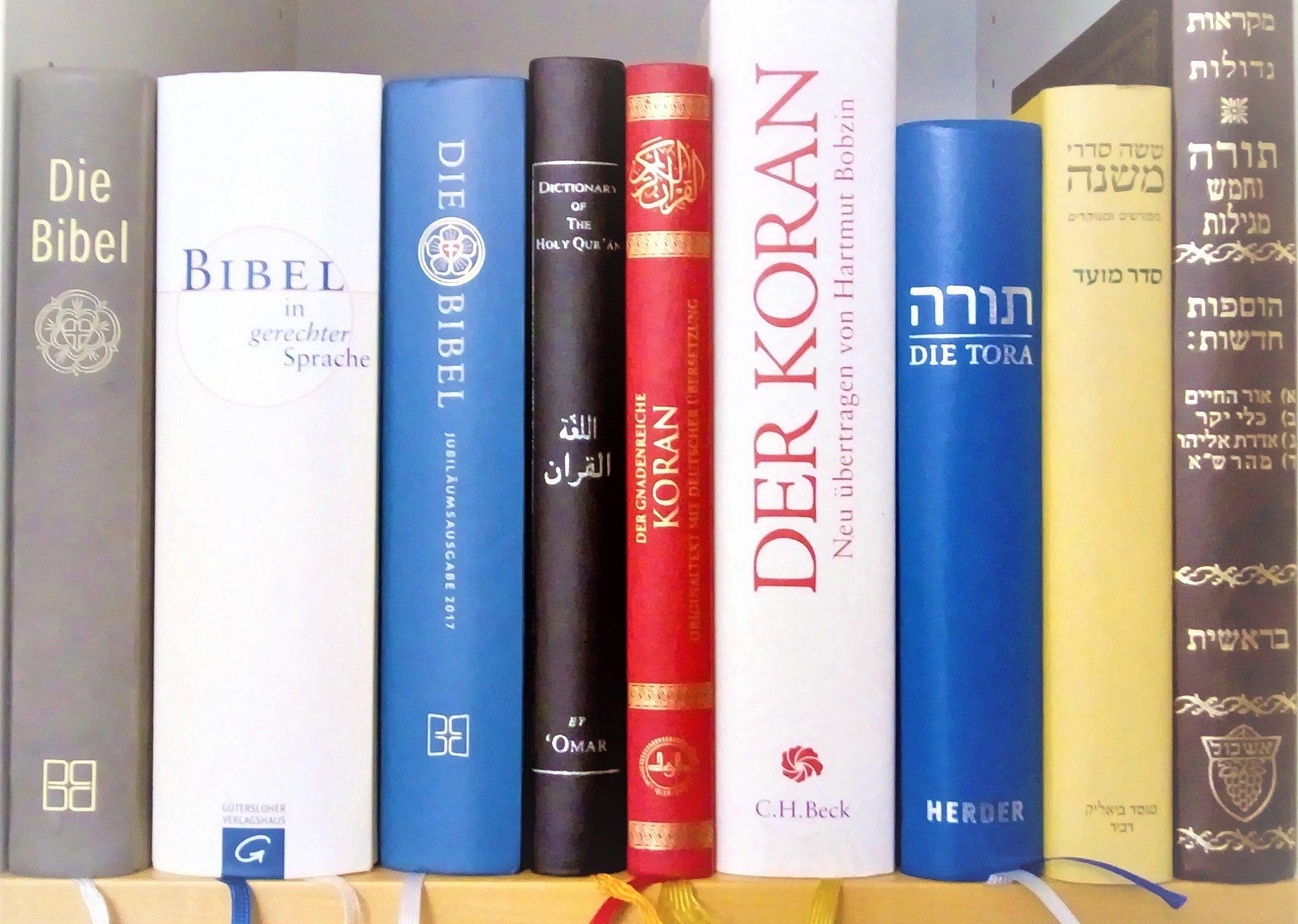 In einen Bücherregal stehen nebeneinander je drei verschiedene Ausgaben der Bibel, des Korans sowie zwei Ausgaben der Tora und eine Mischna