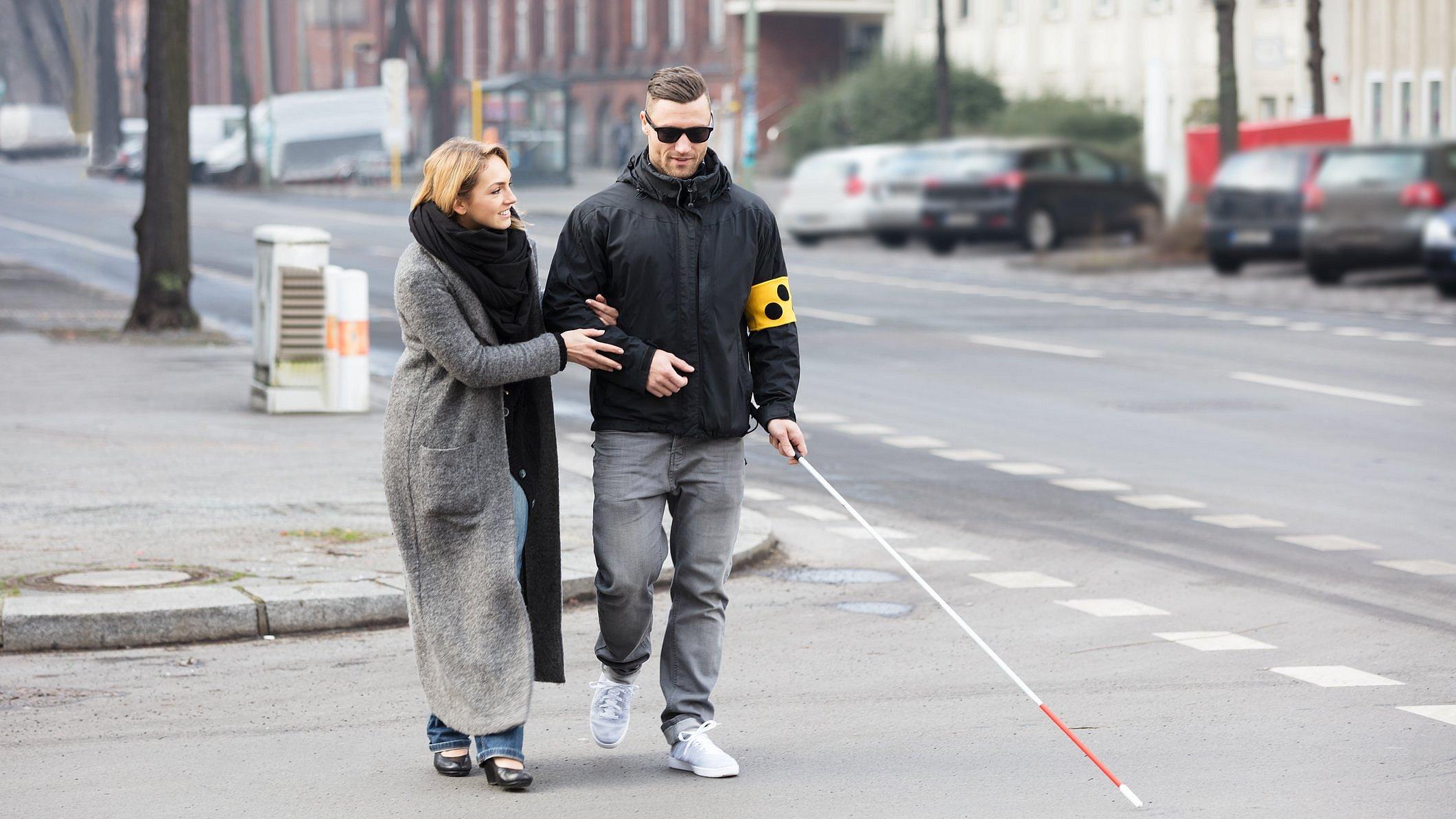 Frau hilft blindem Mann über die Straße