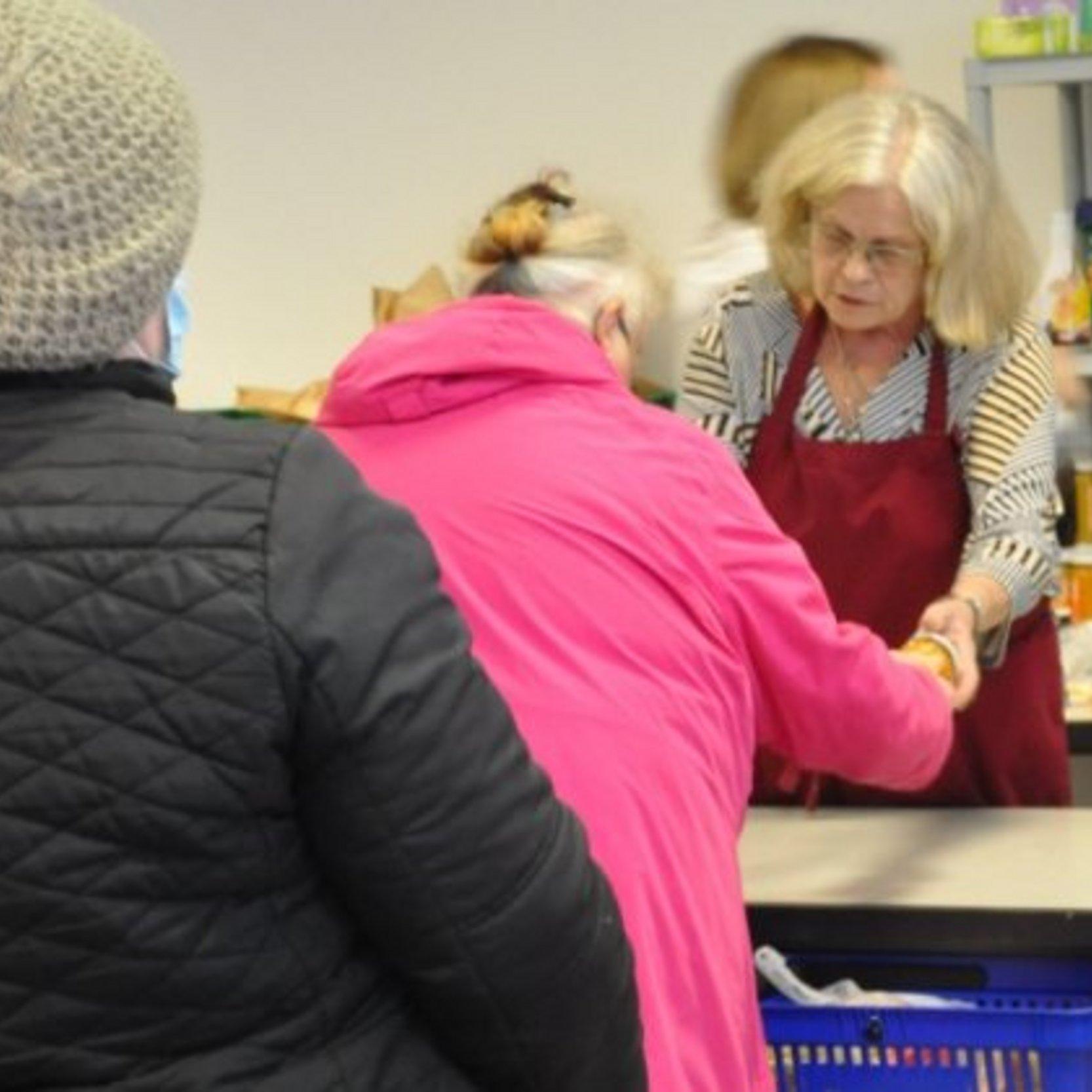 Zwei Frauen holen sich Lebensmittel an der Verkaufstheke ab. In Hintergrund einige kleine Lebensmittelregale