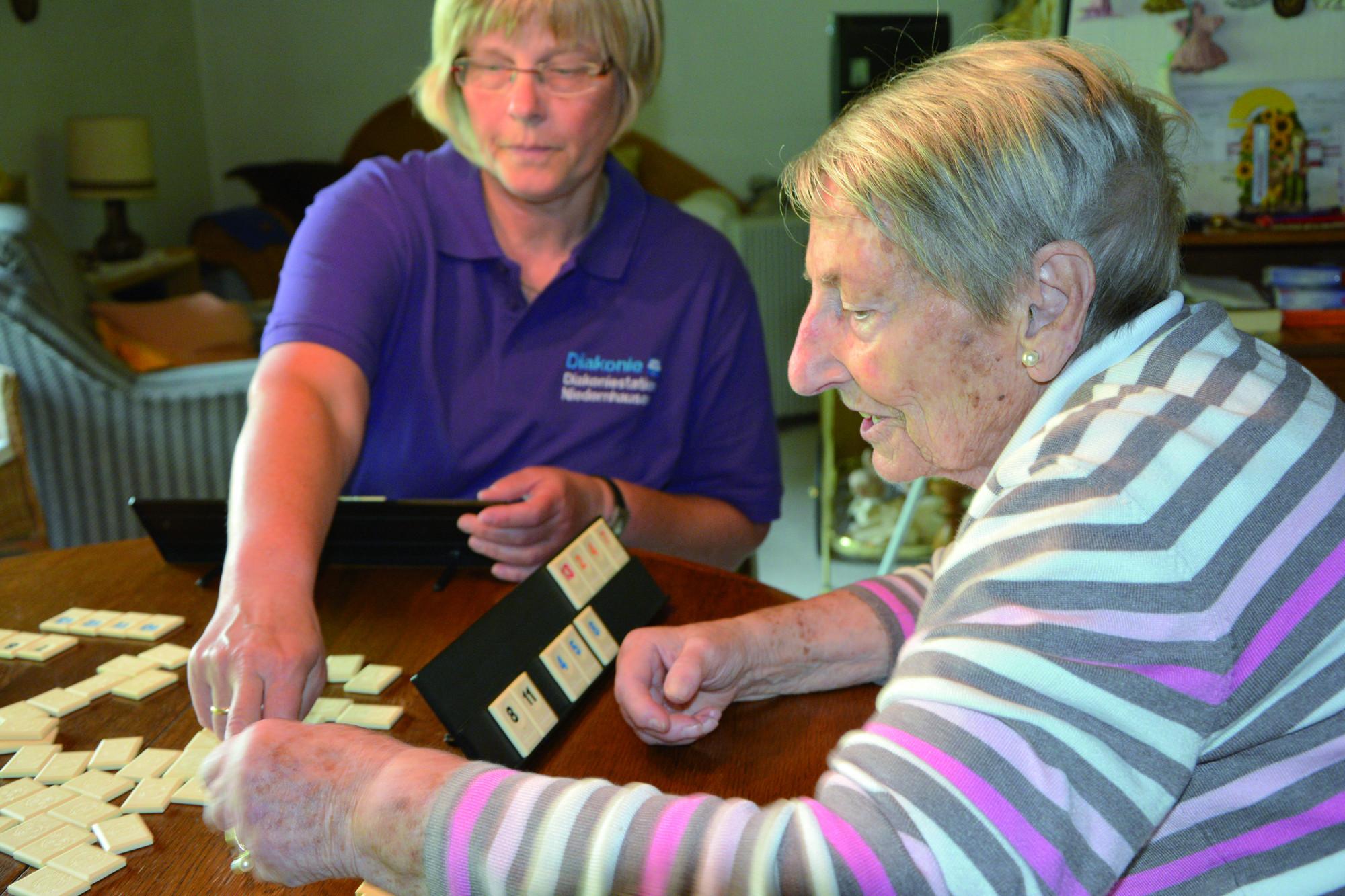 Pflegerin und ältere Damen spielen am Tisch Rummycub