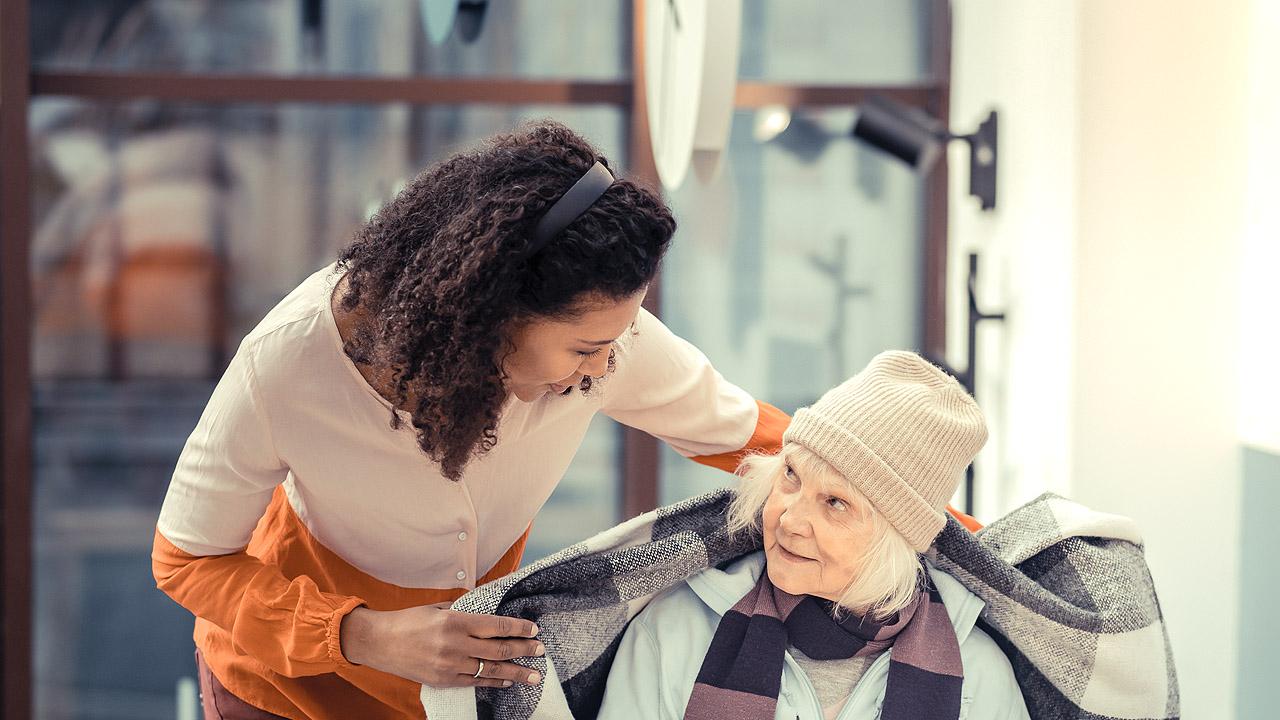 Eine Frau legt eine wärmende Decke um eine alte, obdachlose Frau