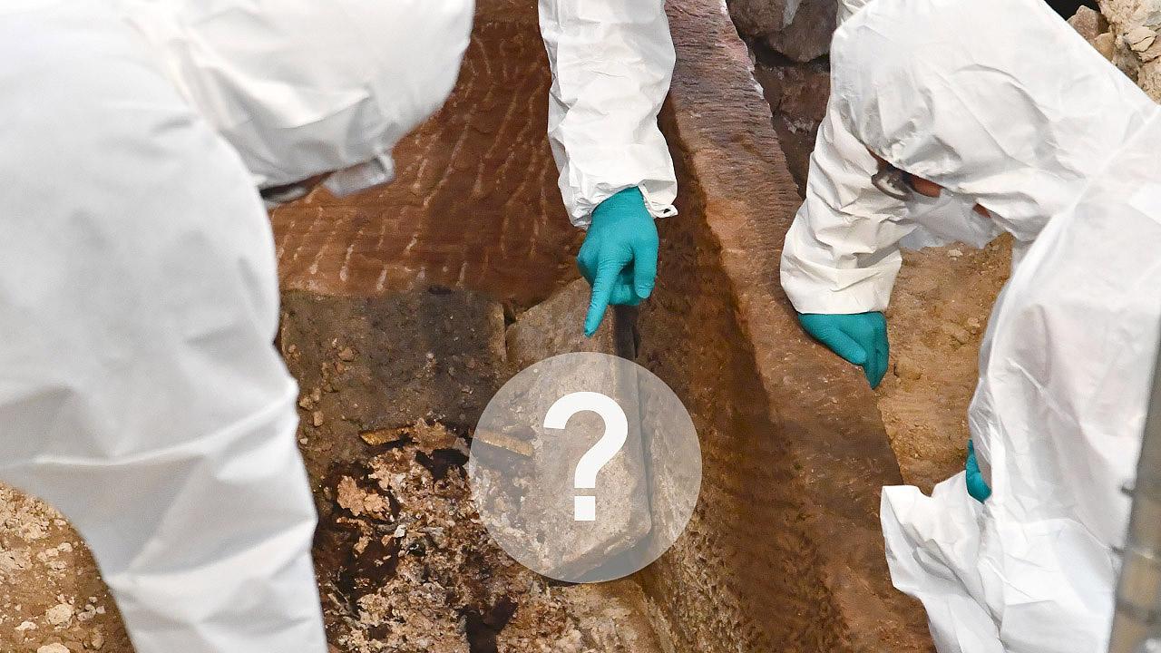 Archäologen in weißen Schutzanzügen zeigen auf eine Fundstelle