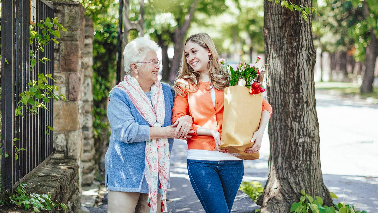 Eine junge Frau hilft einer Seniorin beim Tragen der Einkäufe