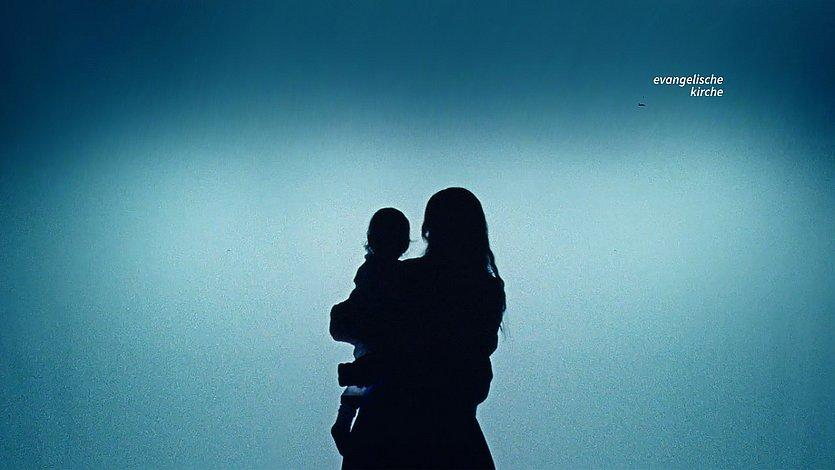 Silhouette einer Mutter mit Kind vor türkisfarbenem Lichtschein