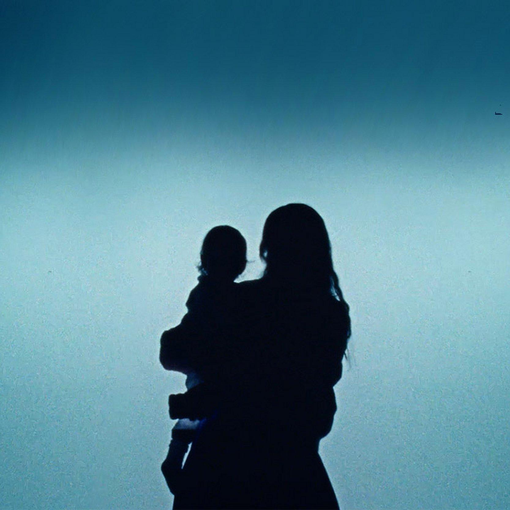 Silhouette einer Mutter mit Kind vor türkisfarbenem Lichtschein