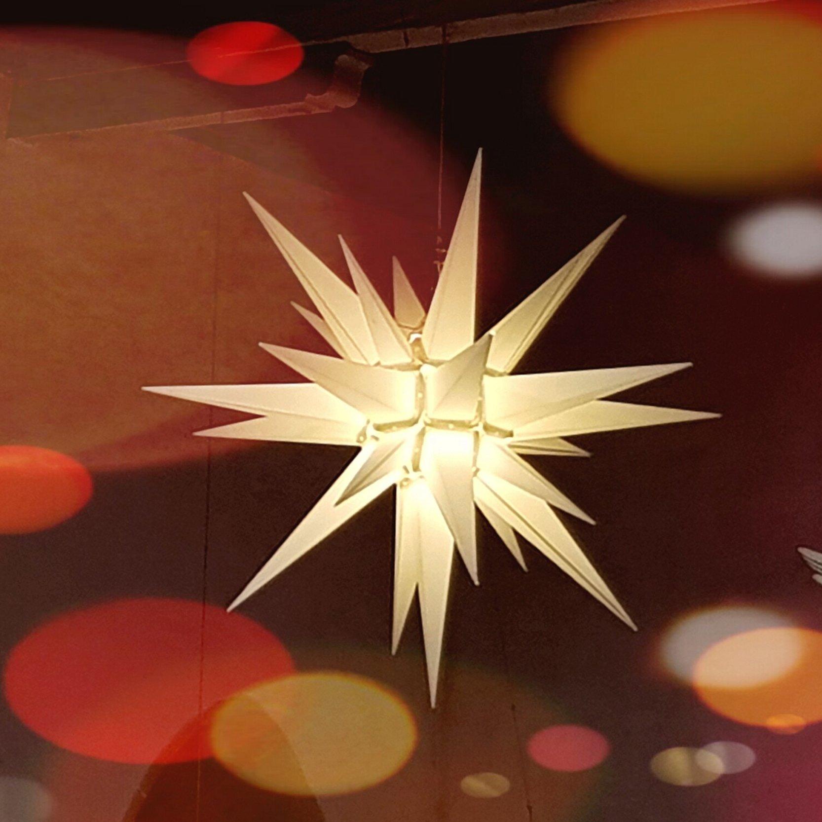 Das Bild zeigt einen weißen Herrnhuter Stern mit bunten Lichtpunkten an der Kirchendecke. In der rechten unteren Ecke ist ein Engel zu sehen.