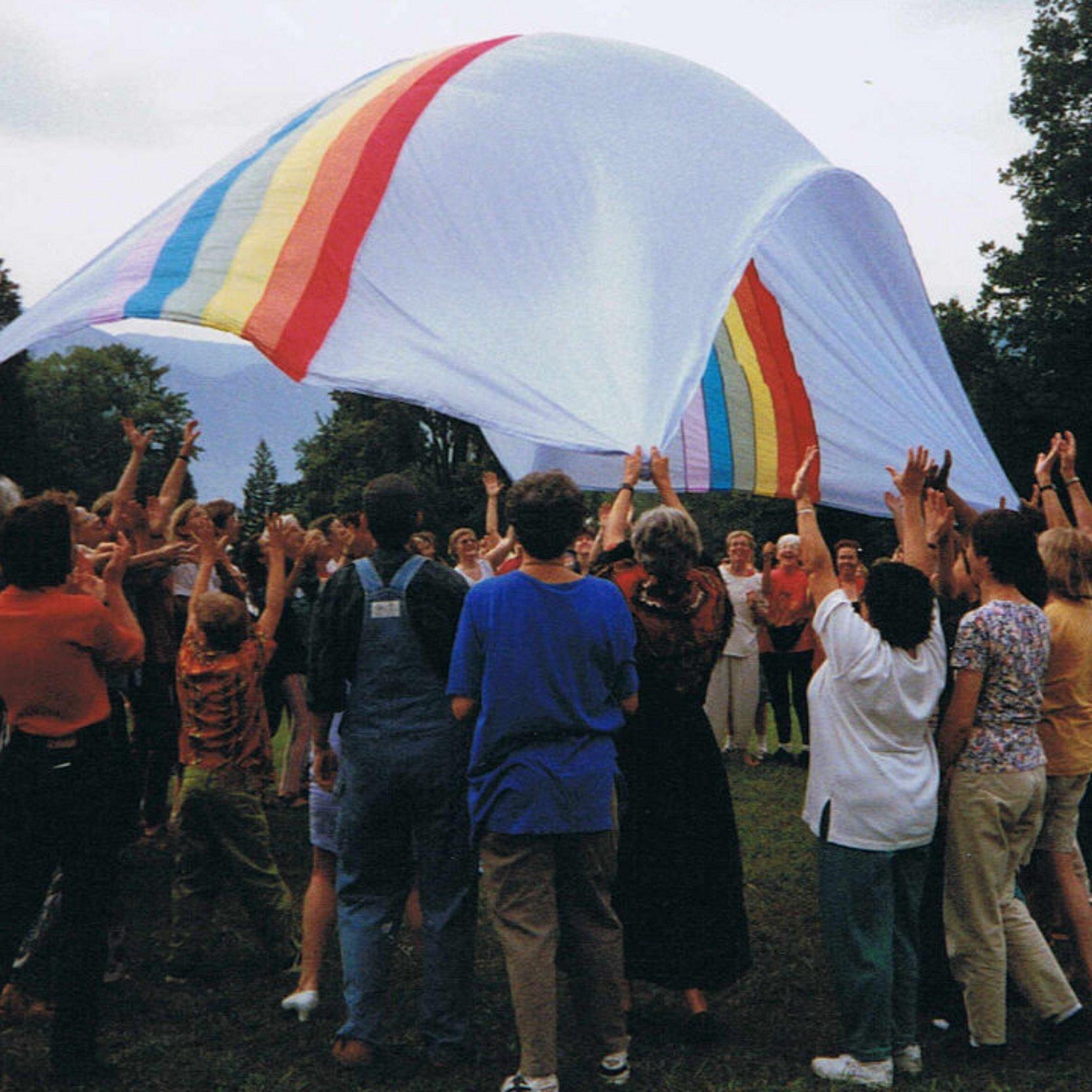 Eine Frauengruppe spielen mit einem Fallschirm in Regenbogenfarben.