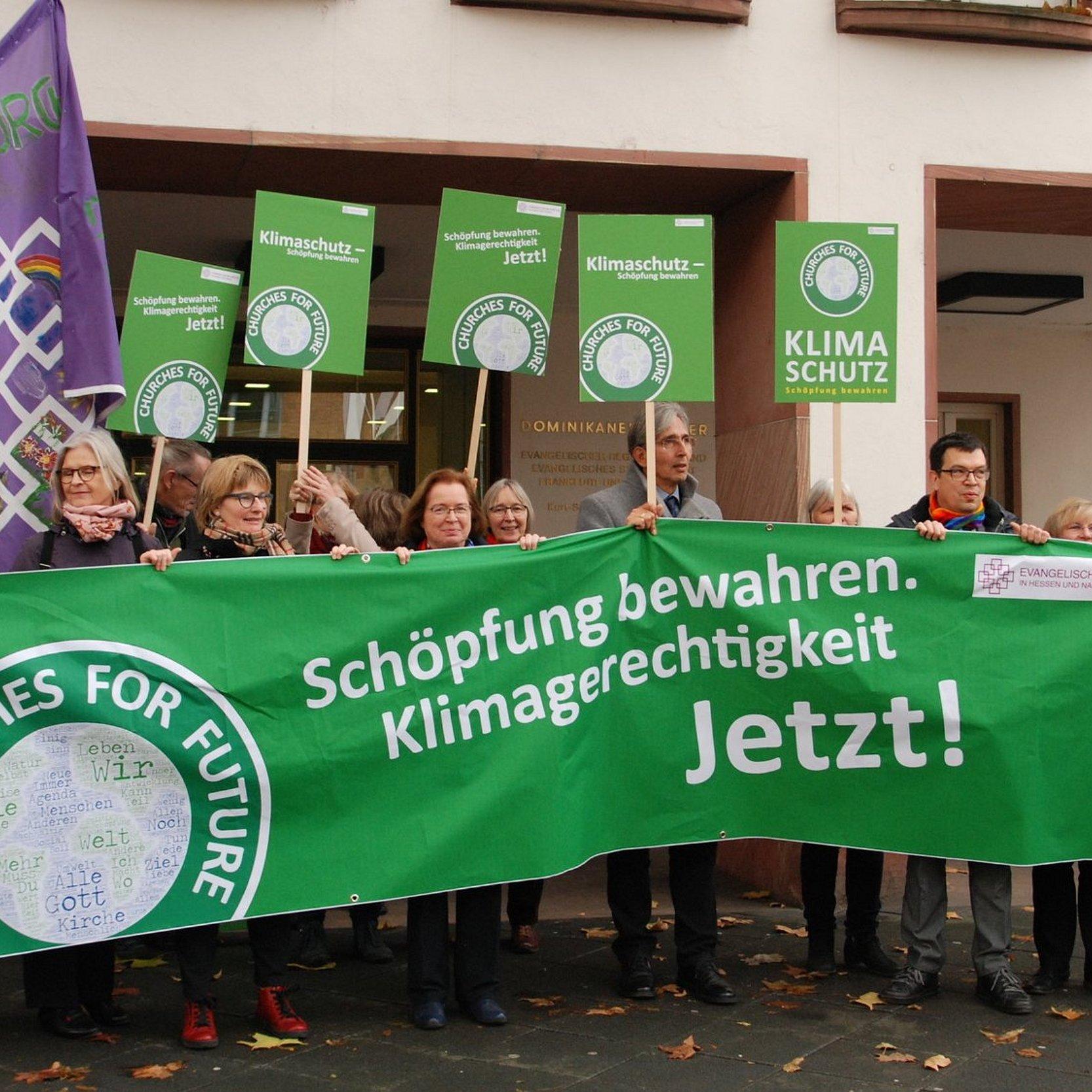 Synodale der EKHN demonstrieren vor dem Dominikanerkloster mit grünen churches for future Bannern und der EKHN-Flagge für Klimaschutz und globale Gerechtigkeit.