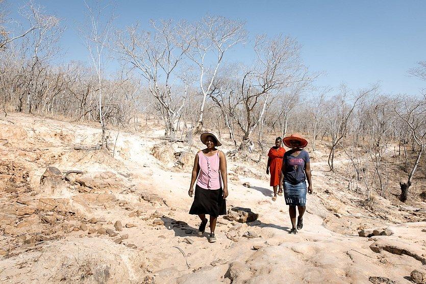 Drei Frauen gehen in karger Landschaft.