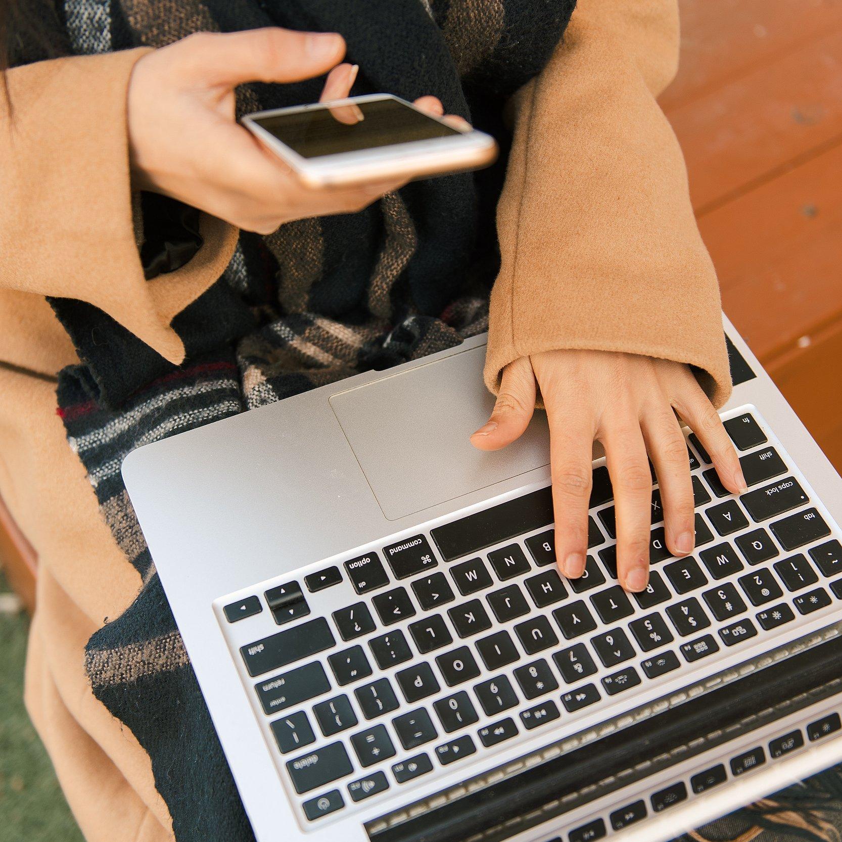 Eine Person bedient Smartphone und Notebook zugleich.