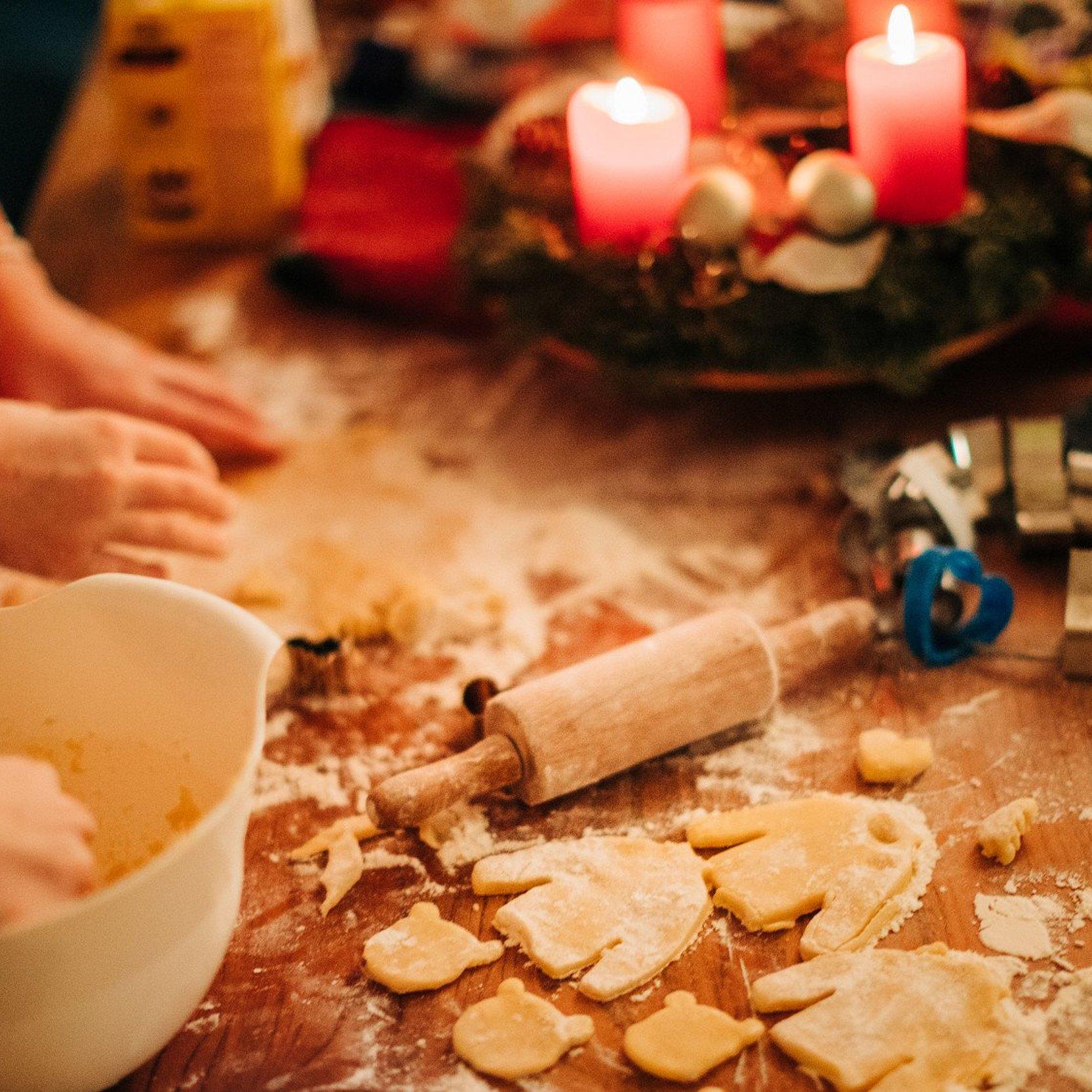 jemand backt Plätzchen, brennende Kerzen am Adventkranz im Hintergrund, eine Schüssel, eine Kuchenrolle