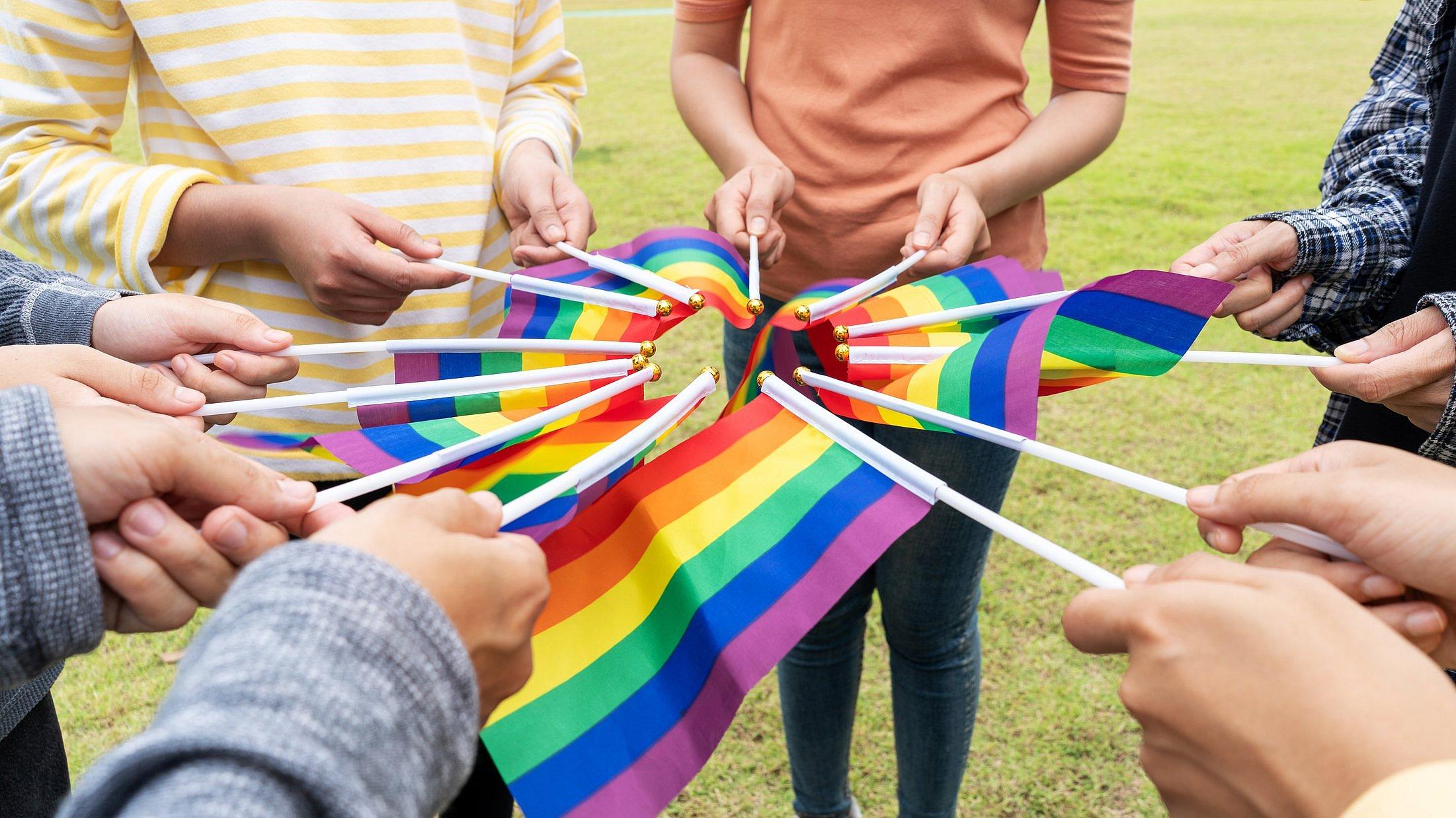 Hände halten Fähnchen mit Regenbogenfarben