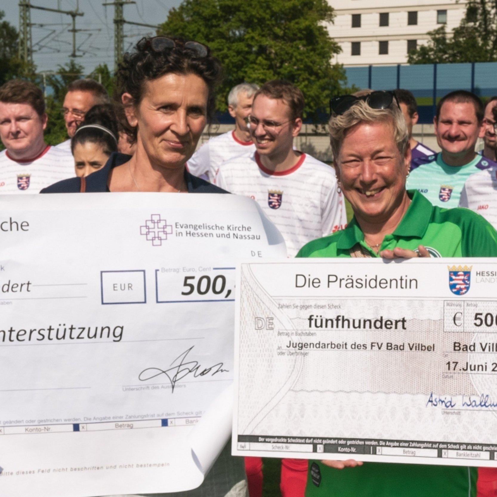 Pröpstin AnkeAnke Spory und Claudia Türk vom FV Bad Vilbel e.V. halten übergroße Spendenschecks hoch.
