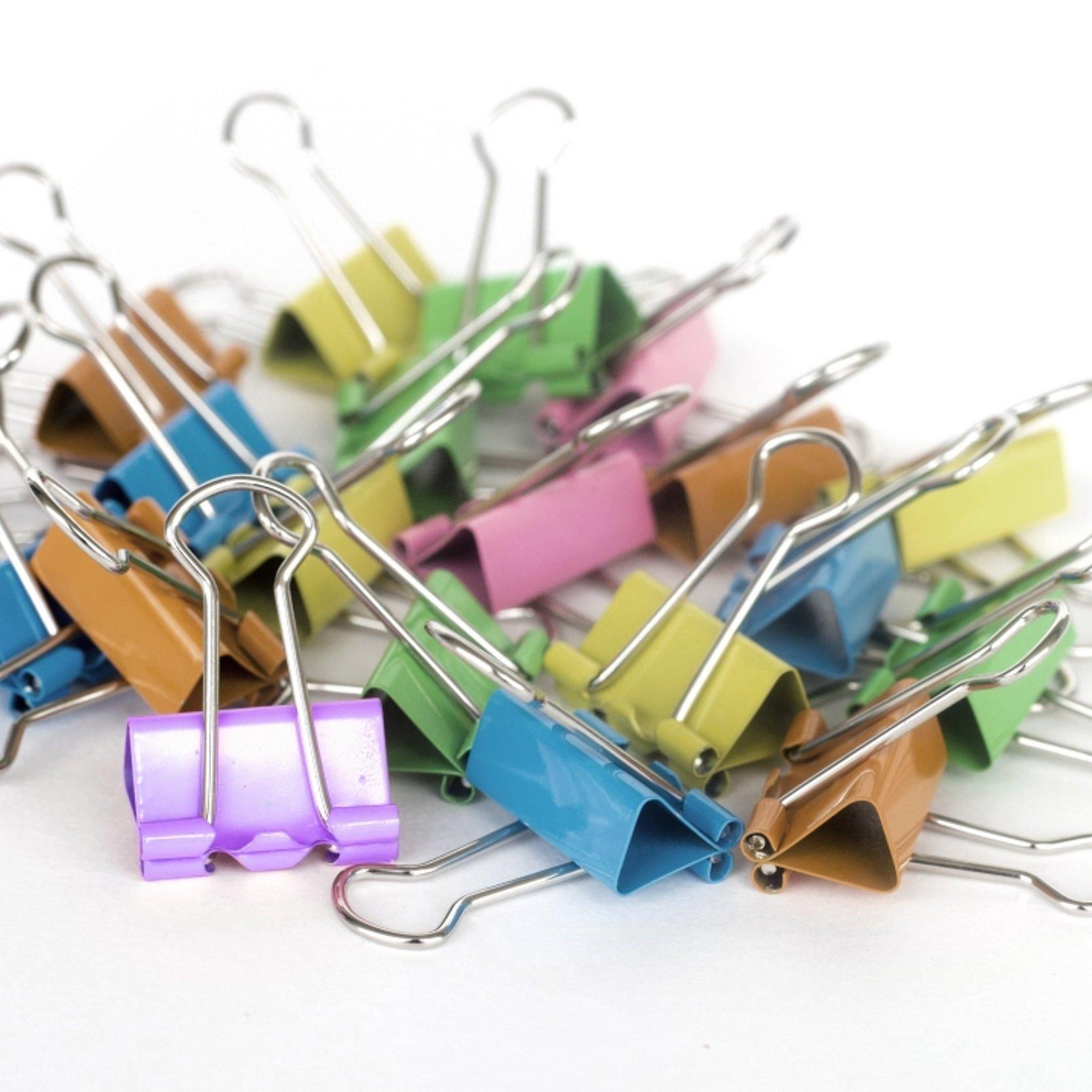 Ein Haufen bunter Foldback-Klammern (Binderclips) in verschiedenen Farben auf hellem Hintergrund.