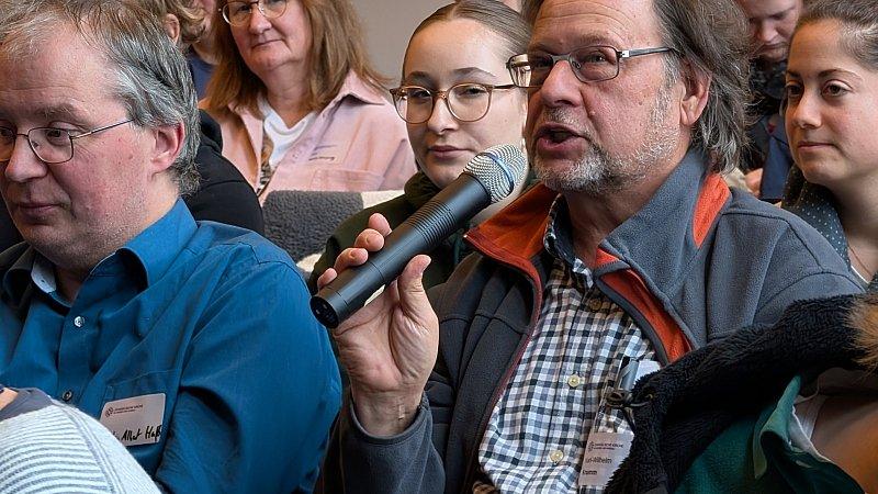 Mann aus dem Plenum spricht ins Mikrofon.