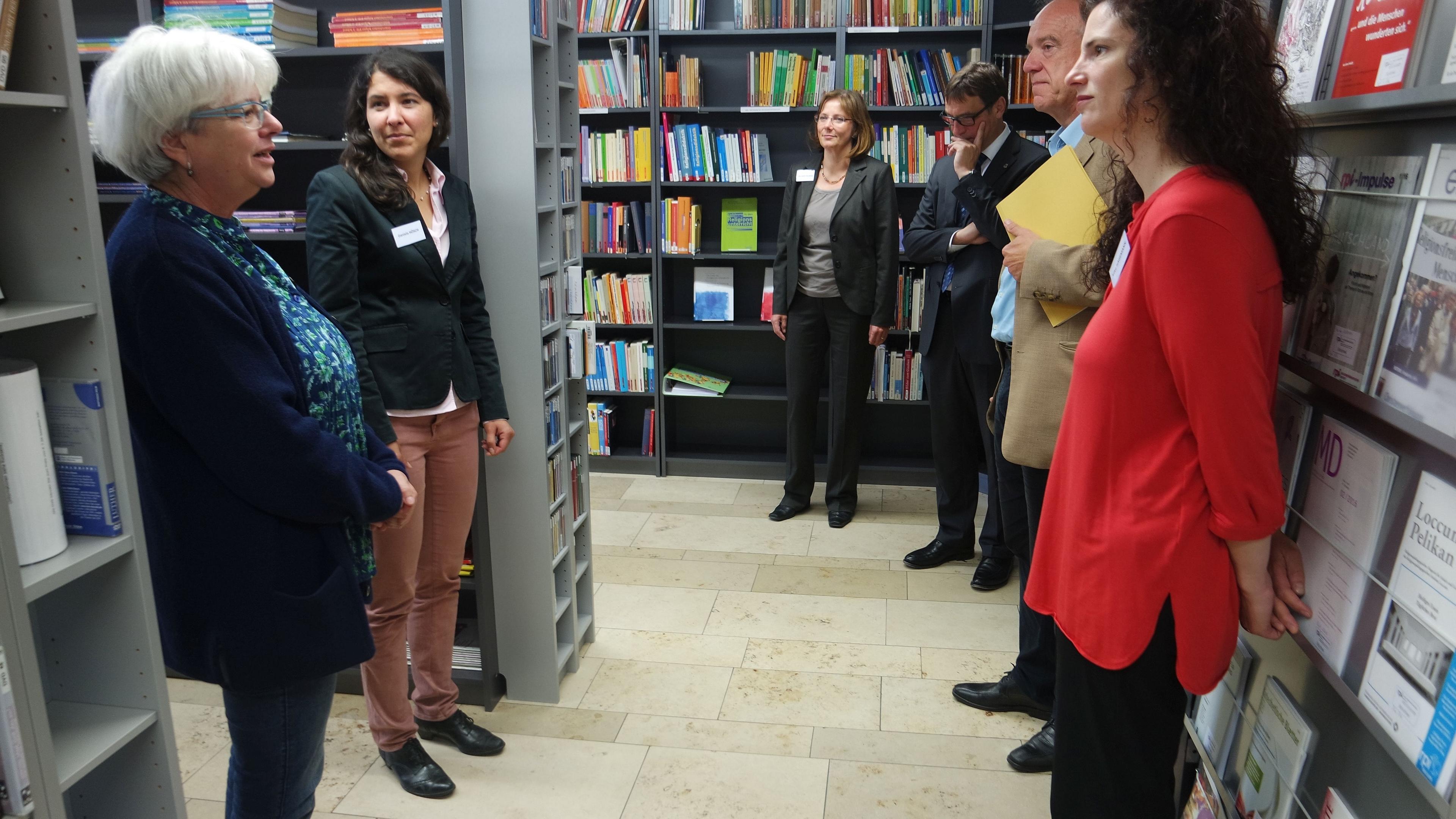 Personen stehen in der Bibliothek zwischen Bücherregalen.