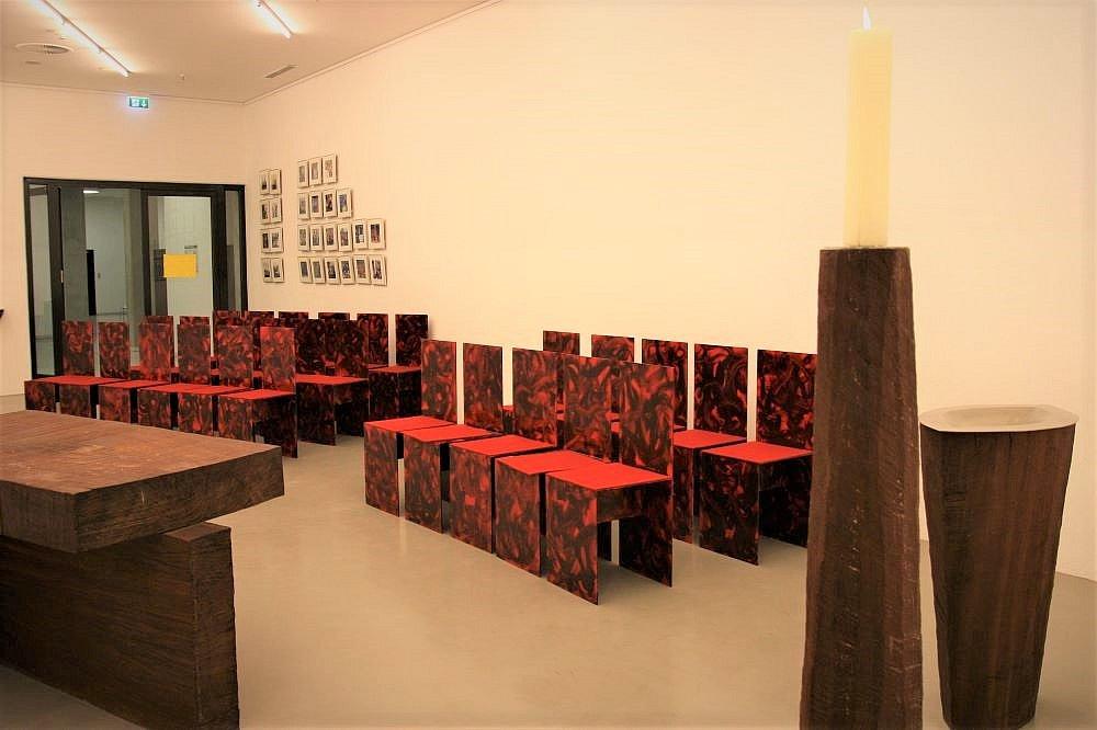 Dieses Bild zeigt den Innenraum der Stadionkappelle mit dem Holzaltar vorne links und zwei Stuhlreihen aus Holz mit roten Sitzauflagen.