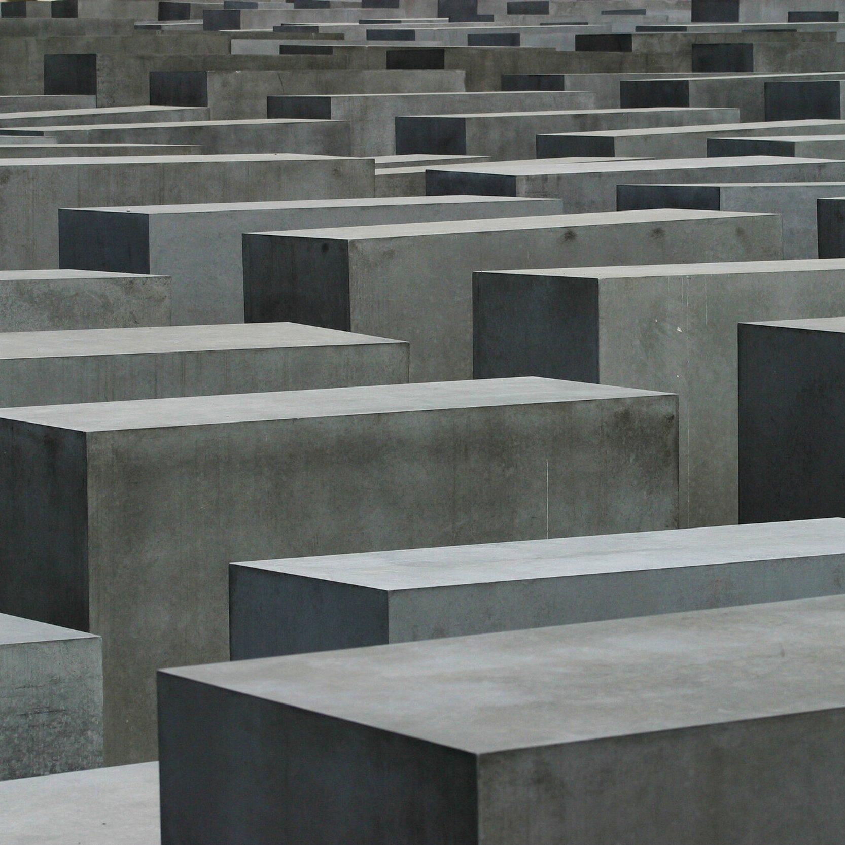 Graue Betonstelen in unterschiedlichen Höhen stehen dicht an dicht in einem rasterförmigen Feld – das Stelenfeld des Holocaust-Mahnmals in Berlin, mit engen Wegen dazwischen und einer nüchternen, beklemmenden Atmosphäre.