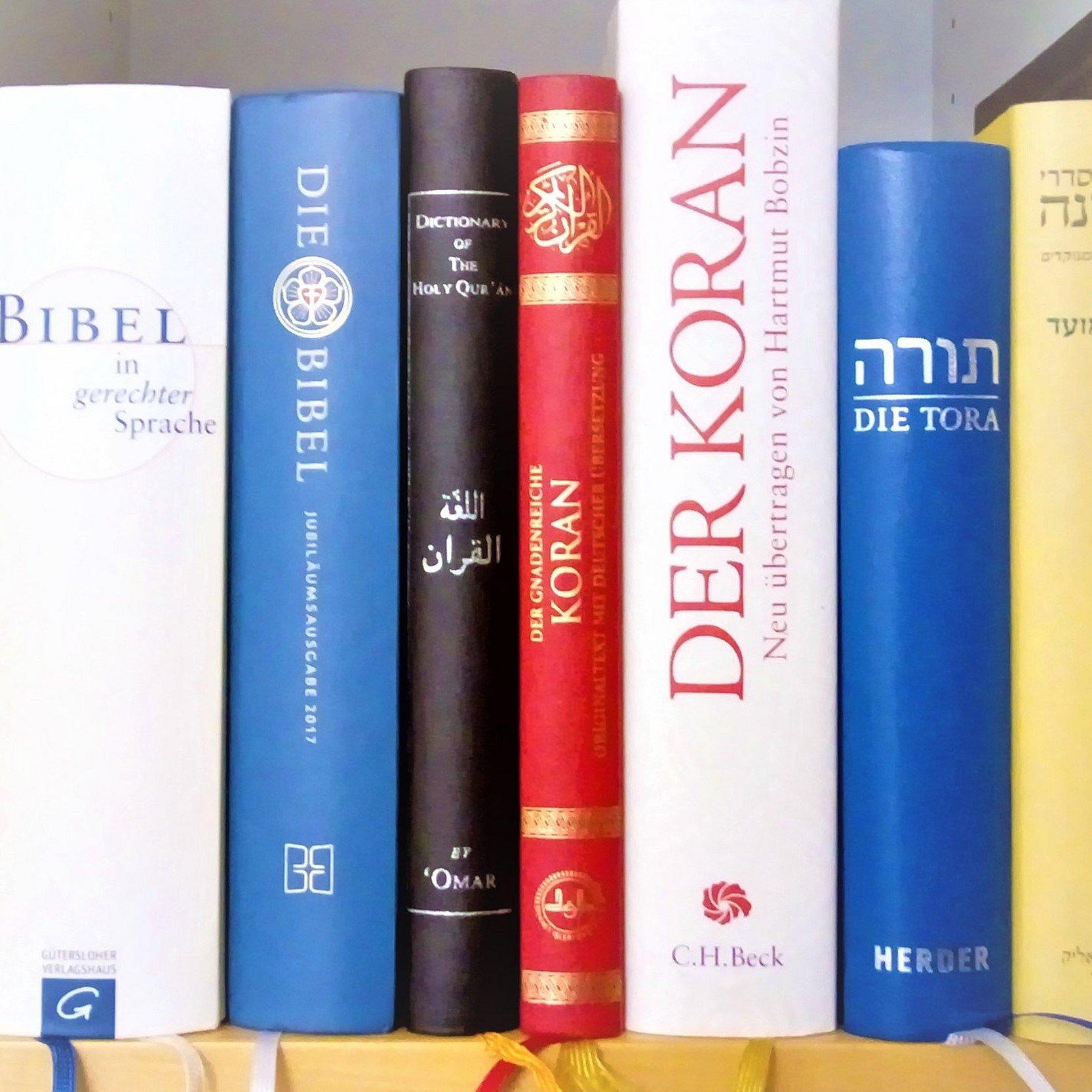 In einen Bücherregal stehen nebeneinander je drei verschiedene Ausgaben der Bibel, des Korans sowie zwei Ausgaben der Tora und eine Mischna