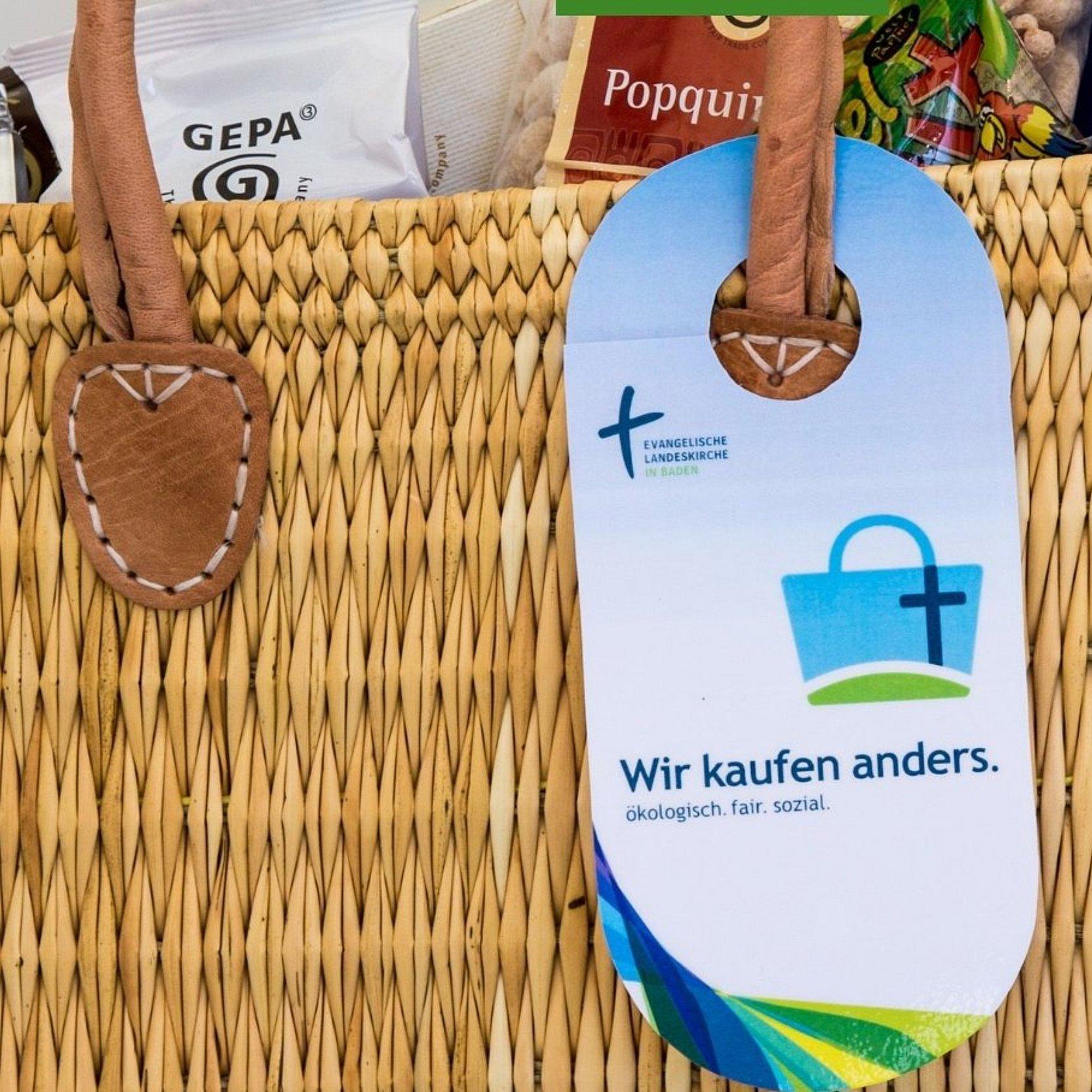An einem vollen Einkaufskorb aus Bast hängt ein Schild: Wir kaufen anders. öko. fair. sozial.