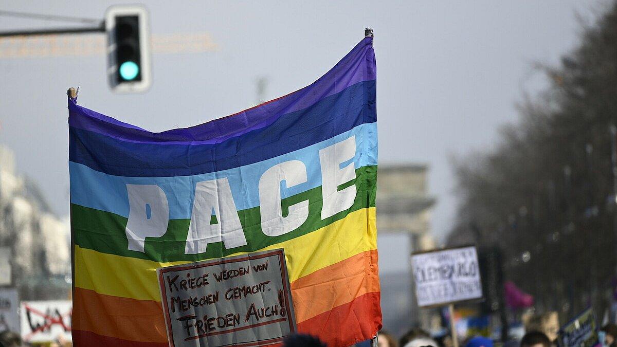 Ein Demonstrationszug gegen den Krieg in Ukraine. Einige der Demonstrierenden halten eine Regenbogenfahne mit der Aufschrift "PACE" hoch.
