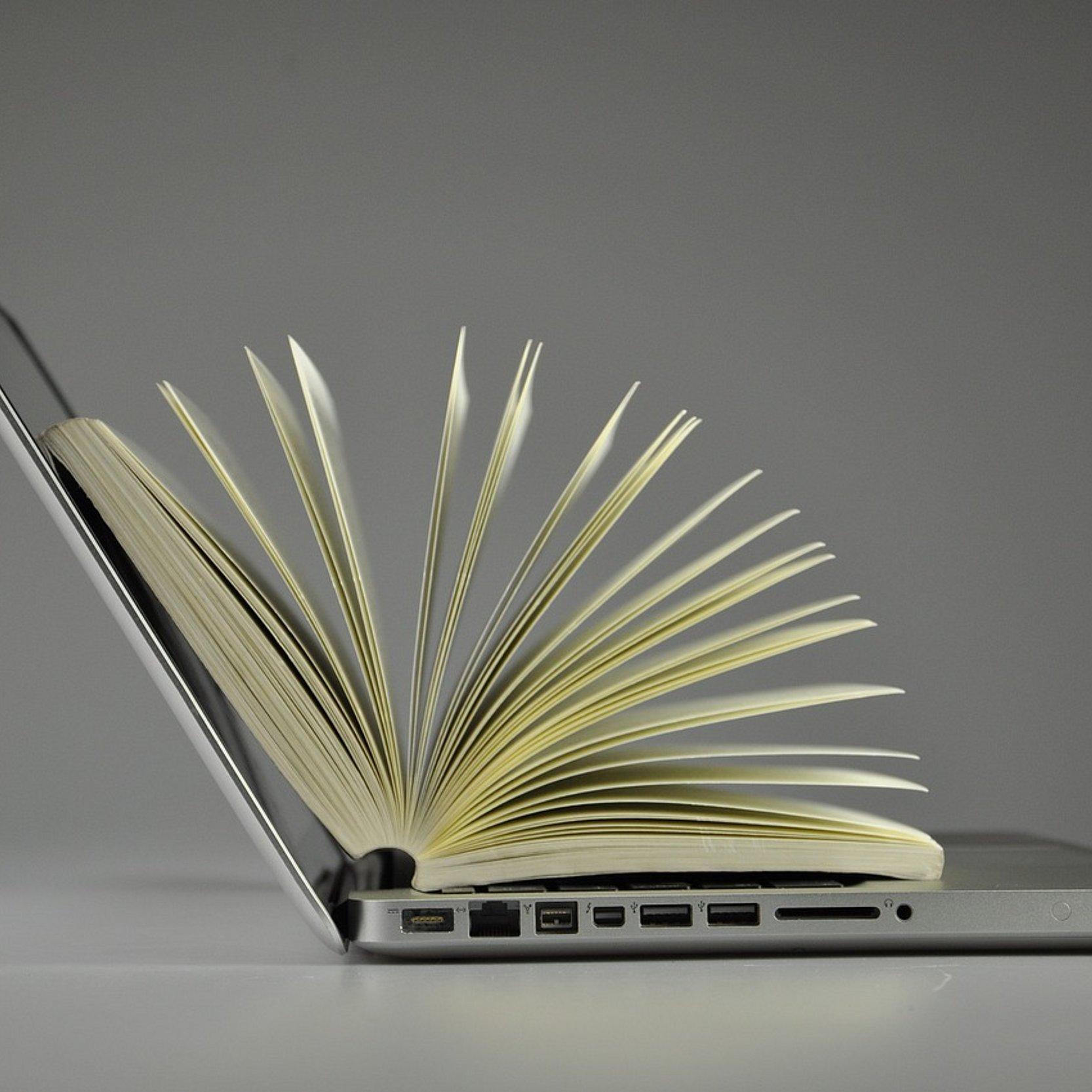 Aufgeschlagenes Buch liegt auf aufgeklapptem Laptop