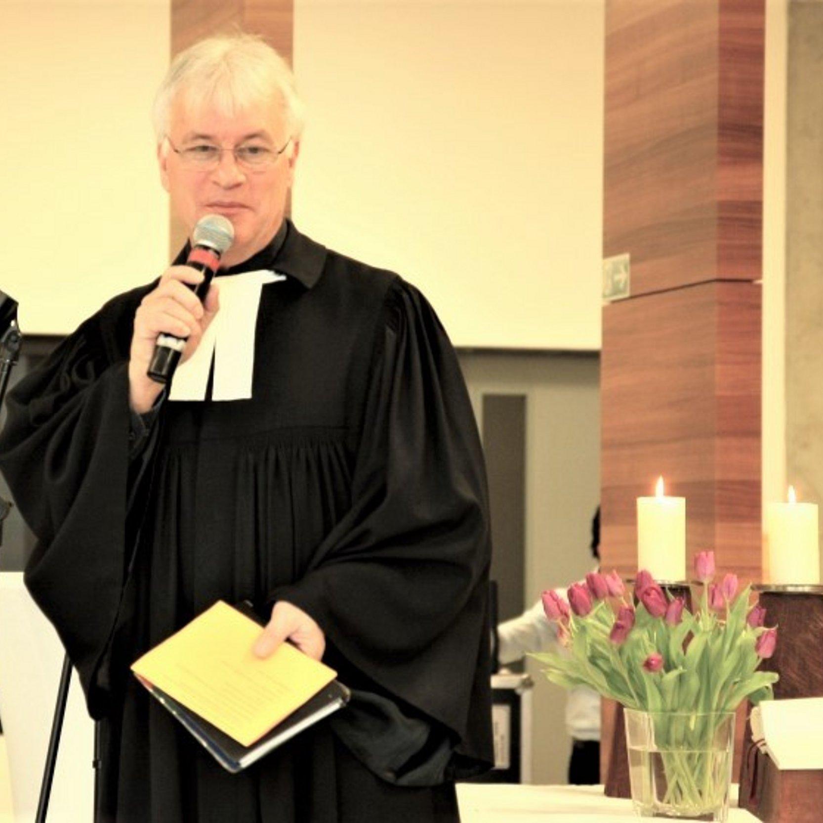 Pfarrer Eugen Eckert mit Mikrofon und Bibel vor dem Altar in der Stadionkapelle