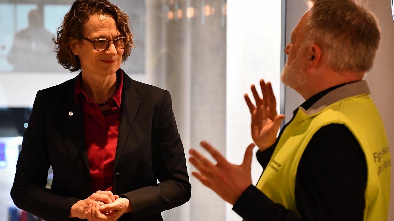 Kirchenpräsidentin im dunklen Blazer und roter Bluse hört aufmerksam einem Seelsorger in einer gelben Sicherheitsweste zu, der mit erhobenen Händen gestikulierend spricht