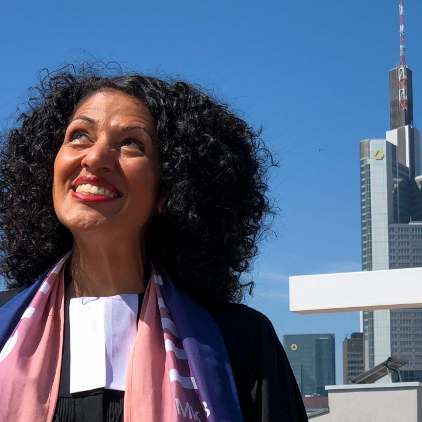 Portrait, im Hintergrund Hochhäuser in Frankfurt und ein Holzkreuz