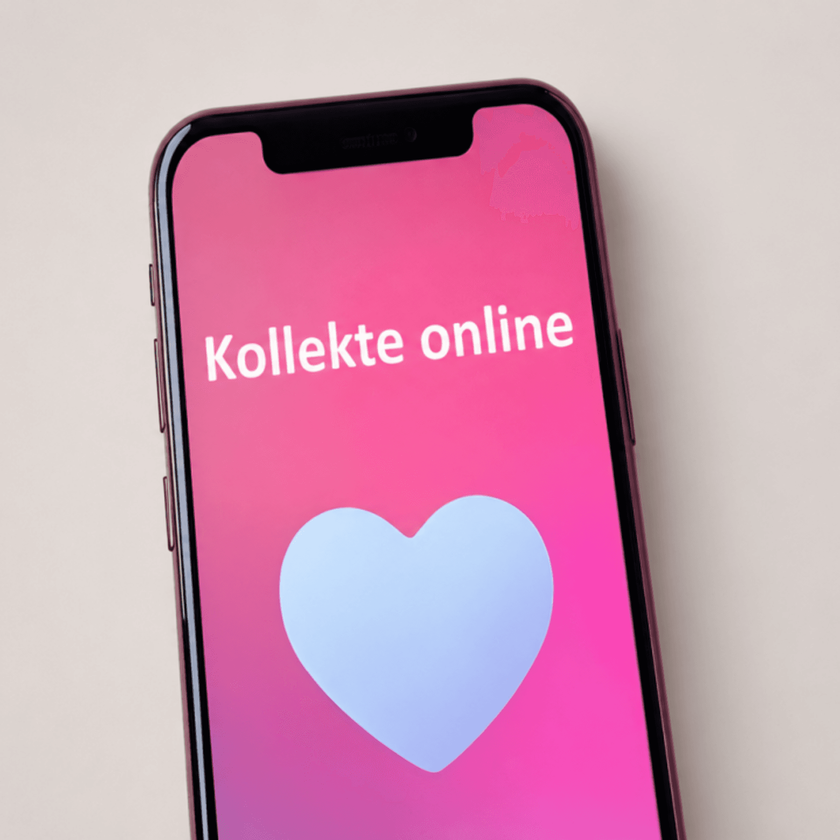 Ein Smartphone mit pinkem Bildschirm und der Aufschrift „Kollekte online“ sowie einem Herzsymbol steht vor einem neutralen, hellen Hintergrund.