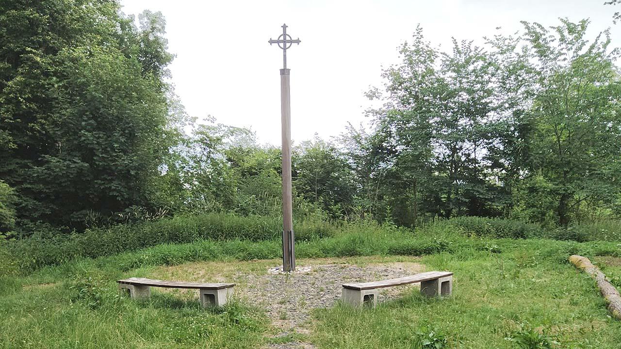 Pilgerkreuz auf einer schlanken hohen Säule, darum Bänke im Kreis