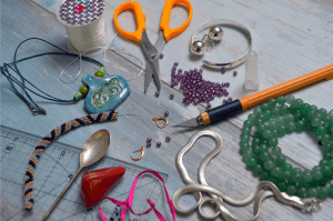 Bastelmaterial: Schere, Perlen, Schnur, Lineal verstreut auf einem Tisch