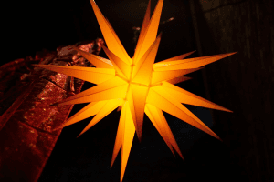 Orange leuchtender Herrnhuter Stern vor schwarzem Abendhimmel