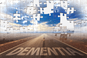 Straße die geradeaus durch eine karge Landschaft führt. Auf der Straße steht groß das Wort "Dementia" steht. Das Bild ist als Puzzle dargestellt, in dem ein paar Puzzleteile fehlen.