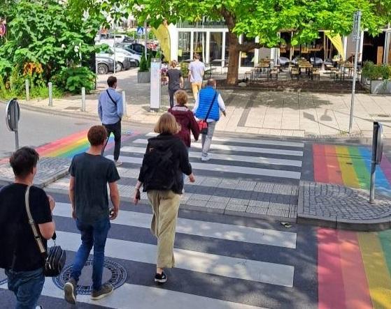 Menschen laufen über einen Zebrastreifen, der vom Pride-Regenbogen gerahmt ist.