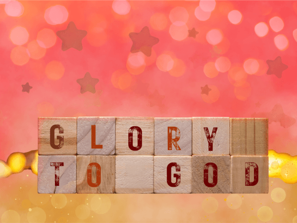 Auf hölzernen Bauklötzen steht "Glory to God". Sie stehen vor einem roten und goldenen Hintergrund mit Sternen.