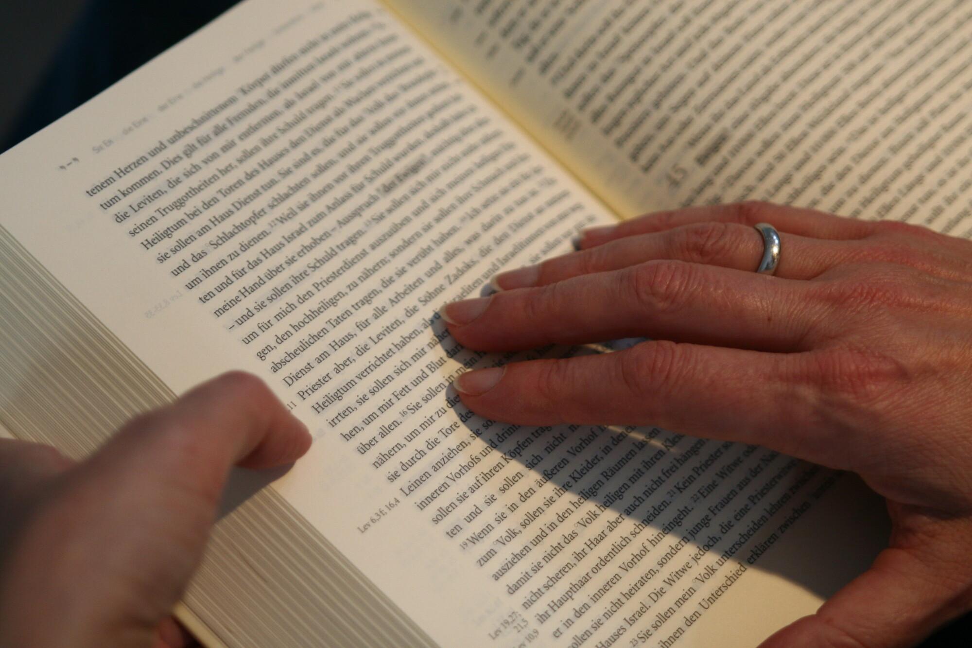 Eine Hand ruht auf einer aufgeschlagenen Bibel und verharrt auf einem Satz.