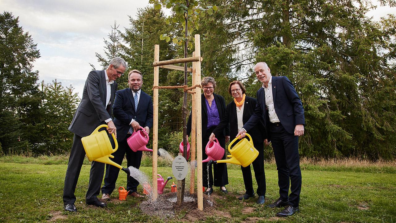 Evangelischen Hochschule Hessen Menschen gießen mit bunten Gießkannen einen jungen Baum