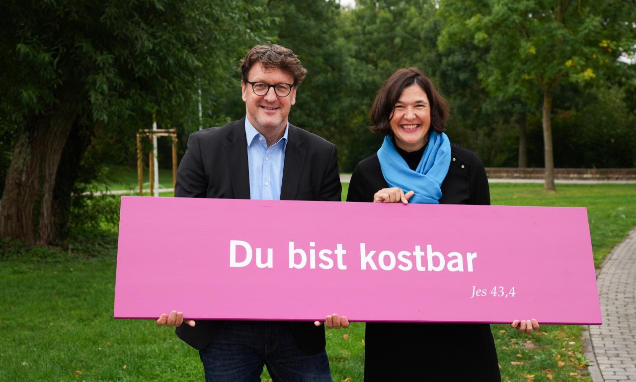 Zwei Personen mit Banner, darauf die Losung "Du bist kostbar"