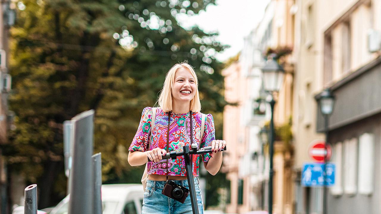 Stadt erkunden Eine Frau mit einem Roller erkundet die Stadt