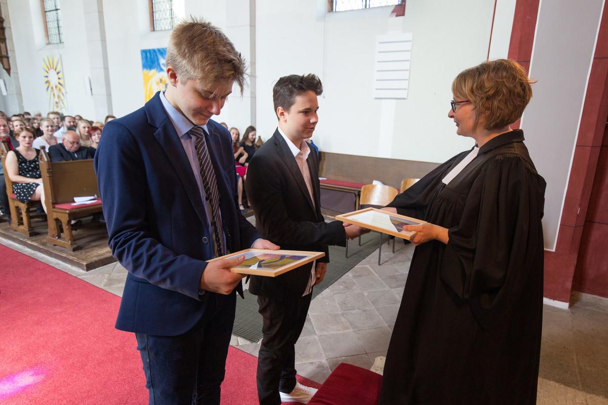 Segenspruch wird übergeben bei der Konfirmation im Gottesdienst Zwei Konfirmanden stehen mit dunklen Anzügen vor der Pfarrerin im Talar. Die Pfarrerin überreicht den beiden den Segenspruch.