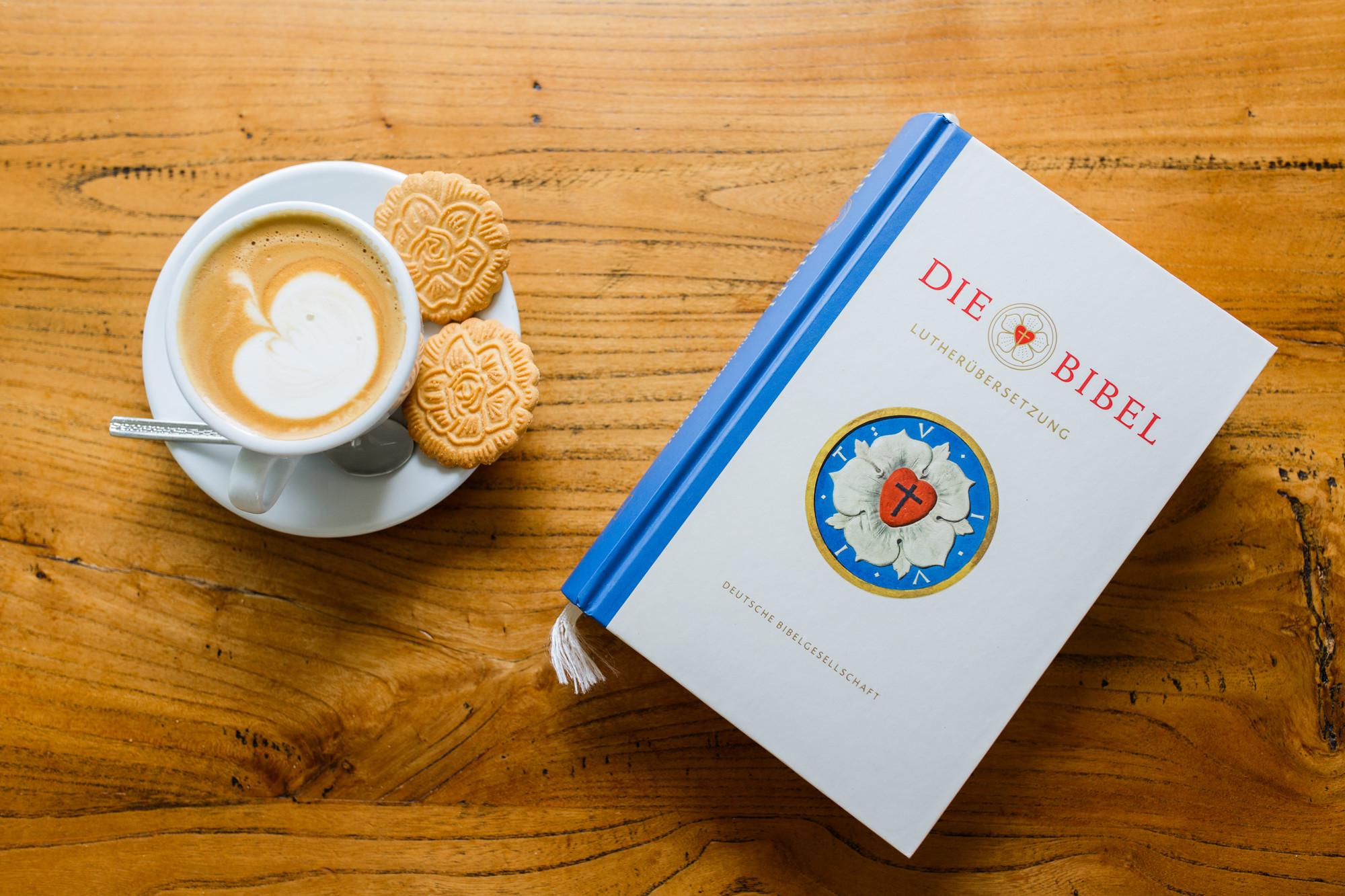 Bibel Lutherbibel neben einer Kaffeetasse mit Milchschaum in Apfelform und Keksen in Form der Lutherrose