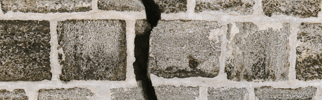 Eine graue Steinmauer mit hellgrauen Fugen, in der Mitte ist ein großer senkrechter Riss