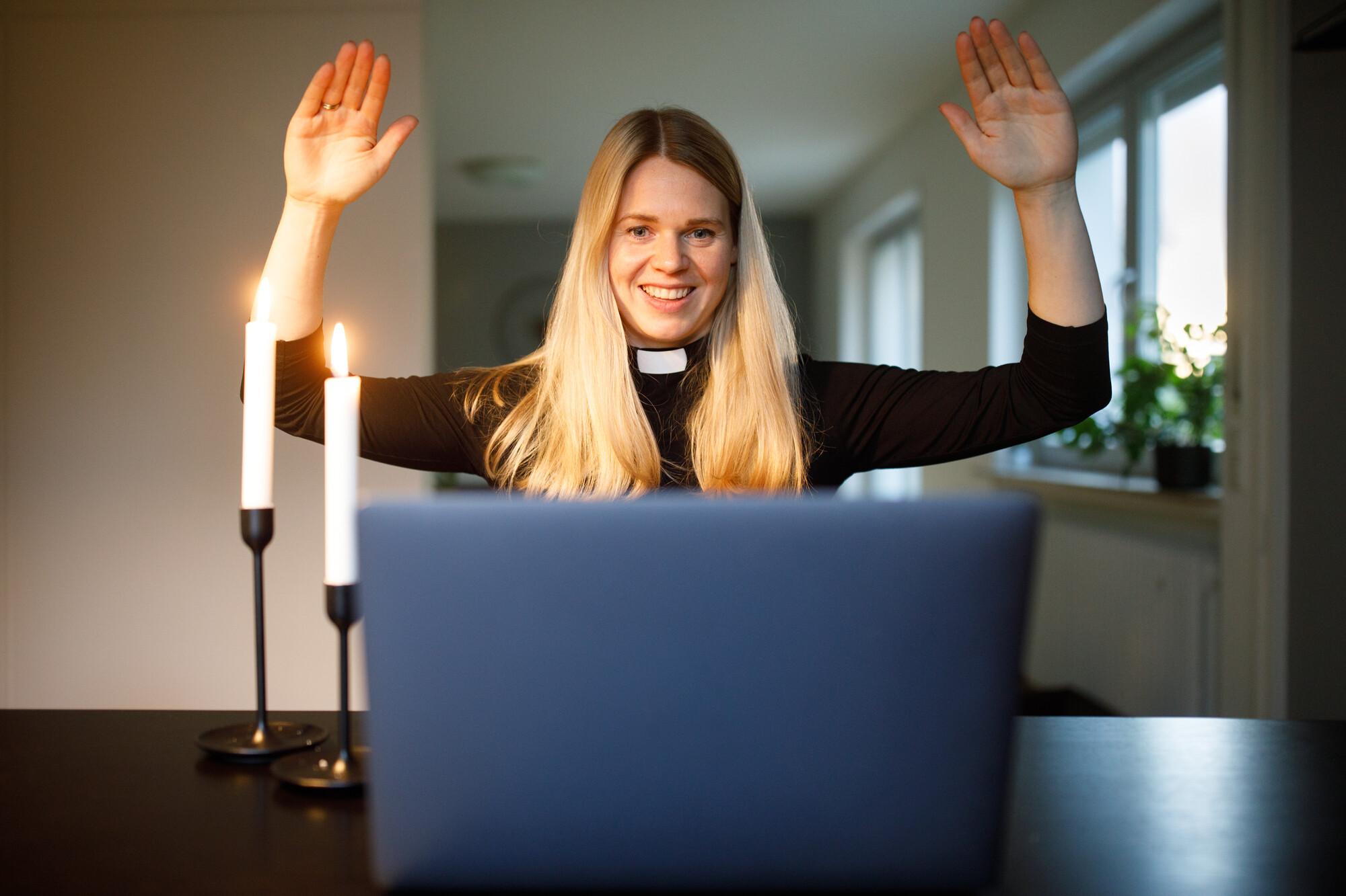 Segen geht auch beim Online Gottesdienst Eine Pfarrerin hält ihre Arme zum Segen hoch während eines Online-Gottesdienstes und schaut in eine Laptop. Zwei Kerzen brenen neben ihr auf dem Tisch.E