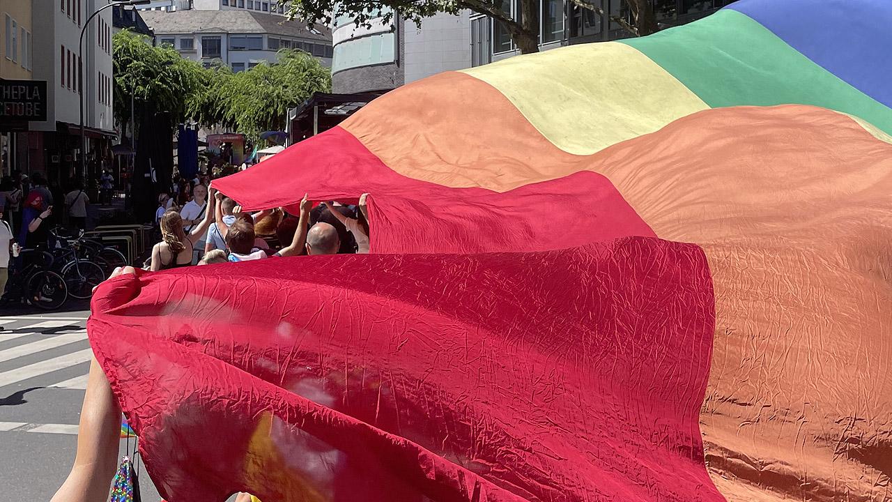 Menschen halten eine riesengroße Regenbogenflagge und sind größtenteils darunter verborgen