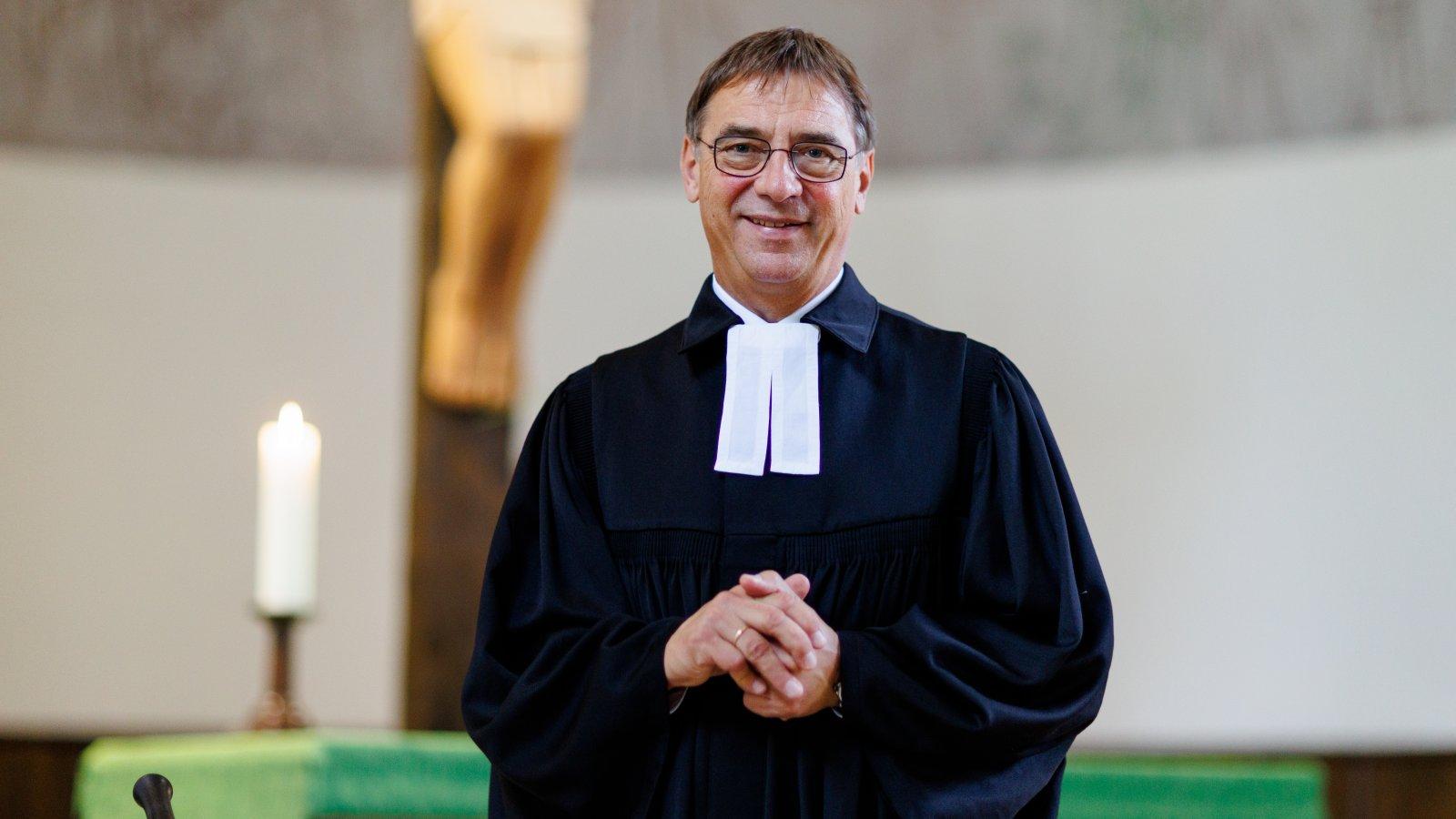 Kirchenpräsident Dr. Volker Jung Portrait, steht vor dem Altar mit einer brennenden Kerze