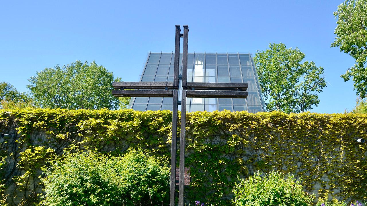 Autobahnkirche Medenbach: Mit Efeu bewachsene Mauer, dahinter ein Kreuz und ein schräges Glasdach