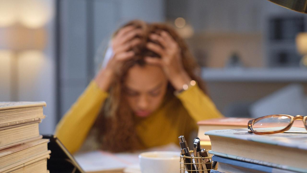 Frau hält ihren Kopf in den Händen, drum herum Bücher
