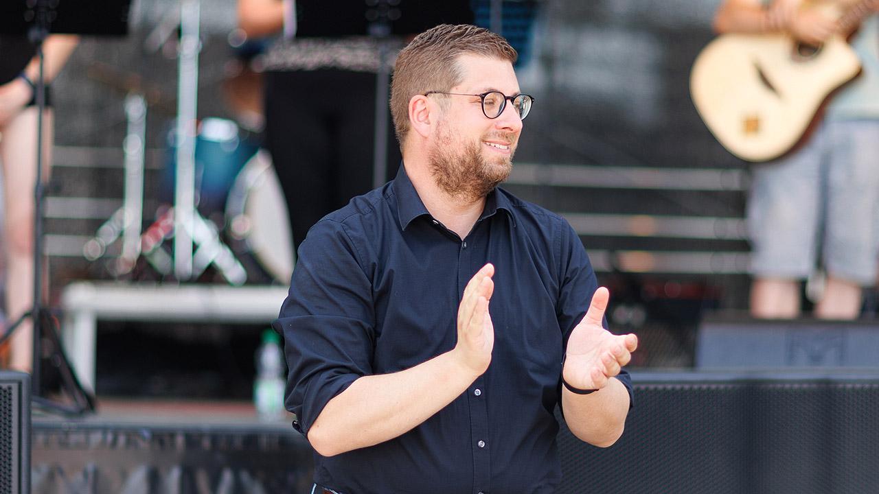 Man sieht den Sinnfluencer und Pfarrer Jörg Niesner vor der Bühne beim Jugendkirchentag, im Hintergrund eine Band auf der Bühne